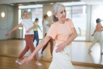 Elderly woman dancing modern dance with people in studio.