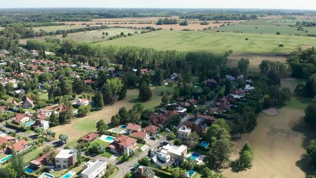 Drone flying backwards revealing wealthy residential area with several detached chalets with private swimming pools in countries of indio cua, Buenos Aires.
