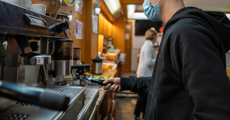 Young guy with a mask making a coffee in a bar machine