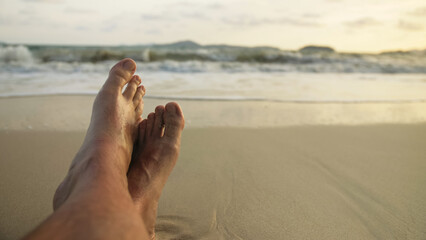 The barefoot man feet relaxed are lying on the sandy beach and washed by the water and foam of the ocean. Concept relax tropical resort traveling happy summer holiday