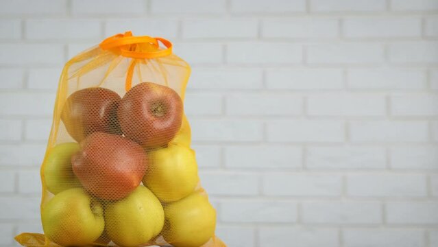 Fresh apples in eco bag. Somebody keep fresh red and yellow apples into a string reusable bag on the table.