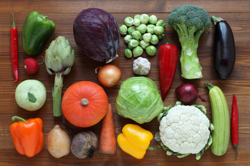 Vegetables on a brown wooden table. Paprika, broccoli, Brussels sprout, kohlrabi, cauliflower, cabbage, red cabbage, squash, artichoke, eggplant, potato, beet, radish, carrot, onion, garlic - Powered by Adobe