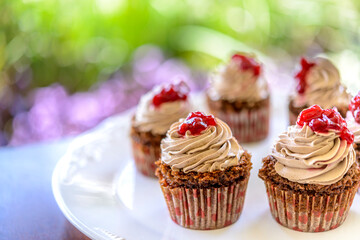 Cupcakes in white plate on wooden table with blurred garden background.