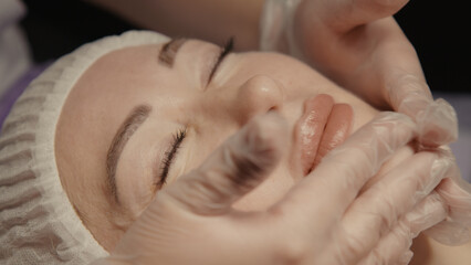 Young hypnotic face woman receiving anti-ageing facial massage in spa salon relax. Wellness body skin care face beauty treatment, rejuvenation procedure getting head face massage. Black background