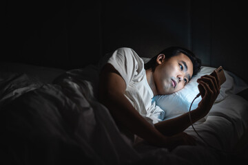 Young man lying on the bed using mobile phone in the dark 