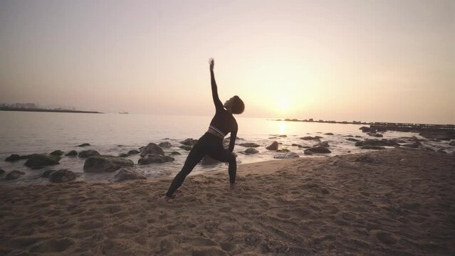 Black afro woman practicing yoga at sunrise on sandy beach, mindfulness meditative asana poses workout for healthy morning routine