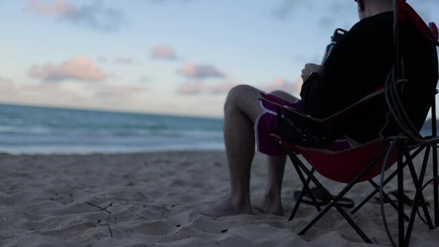 young caucasian man sitting in a beach chair on the sand and watching the surf and waves in hawaii