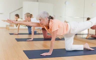 Poster Active senior woman exercising stretching workout and incline during yoga class in fitness studio © JackF