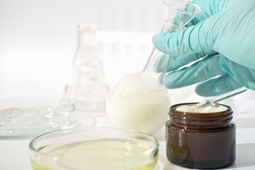 hand in rubber medical glove holding laboratory glassware with fermented cosmetic product, face cream with enzymes developed in a lab.