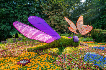 Beautiful dragonfly and butterfly figure standing in multi colored flowers at annual exhibition on...