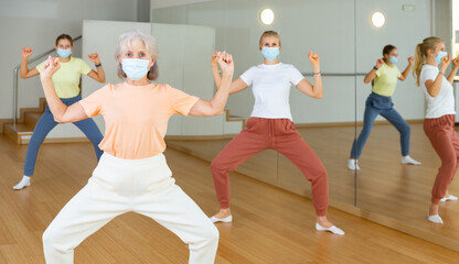 Fototapeta premium Mature woman in face mask dancing with other women during group class in dance center
