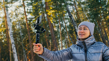 The Woman Professional Videographer Holding Smartphone on 3-axis Gimbal Stabilization Device in Winter. Pro Equipment Helps to Make High Quality Video on Phone. Cinematographer Operator. Slow Motion