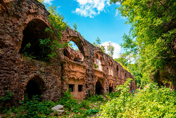 Fototapeta na wymiar Ruins of abandoned old fortification fort surrounded by green plants on sunny day, Remains of ancient old castle against sky