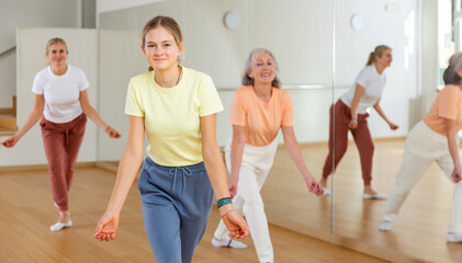 Fototapeta na wymiar Positive teen girl with family doing aerobics exercises with group of people in dance center