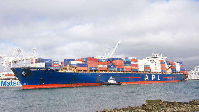 Oakland, CA - Feb 14, 2022: Tugboat REVOLUTION assisting APL cargo ship PRESIDENT CLEVELAND maneuver into the Port of Oakland, the fifth busiest port in the United States.