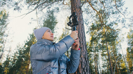 Woman Holding On Handheld Film 3-axis Gimbal Stabilization Device in Winter for Smartphone. Girl Blogger Make Selfie, Broadcast Video Blogging, Vlogging. Videographer Operator Take Photo Video.