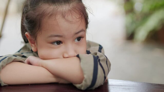 Asian kid girl is sitting on the table and lying down alone outside. Her face expresses sad, unhappy, depressed and thinking emotion which might be caused by stressfulness from school of child.