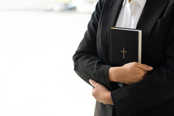 Close-up of black leather with a Christian cross in the hand of a woman in black holding a Bible in...