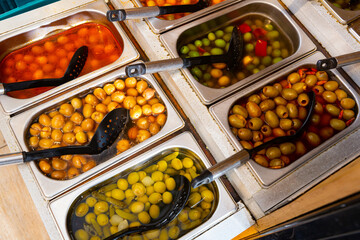 Variety assortment diverse of fresh healthy tasty green and black olives in bowls for sale on market. High quality photo