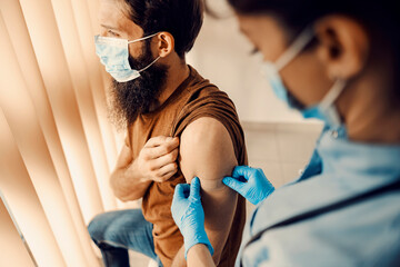 Nurse's hand putting patch on a patient's shoulder after covid 19 vaccine. 