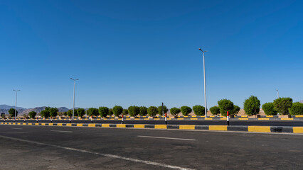 The highway is covered with new asphalt. The marking lines and the dividing barrier are visible. A row of green bushes along the road. Mountains against the blue sky in the distance. Egypt. Safaga