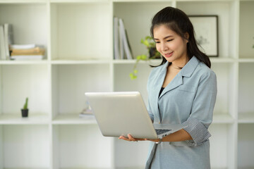 Female manager standing in office and holding an open laptop computer.
