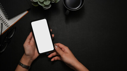 A female hands holding smartphone mockup over black workspace