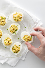 Creamy deviled eggs on a glass plate with a hand taking one.