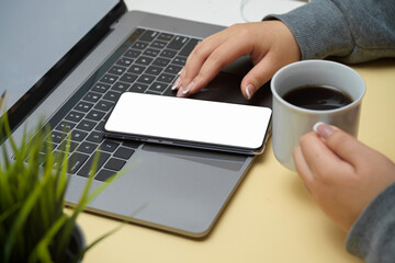 Female in grey sweater sipping black coffee and using smartphone
