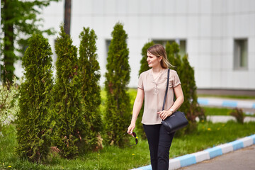 young woman walks down the street of a green city on a sunny summer day.