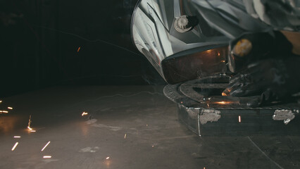 Forge workshop. Smithy. Worker in a welding hood helmet welds a part by electric welding. Sparks...