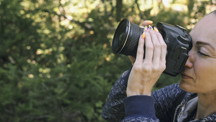 Fototapeta premium Traveler photographing scenic view in forest. One caucasian woman shooting close up look. Girl take photo video on dslr mirrorless camera. Professional photographer travel with backpack. Outdoor.
