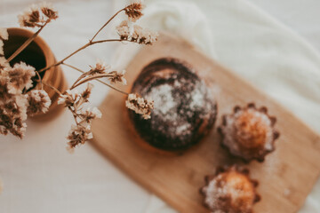 muffins and a bun with chocolate sprinkled with powdered sugar on a wooden background. Blurred background.