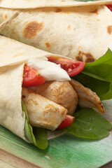 Selective focus on wrap tortilla of arugula, tomato, grilled chicken and cream cheese.