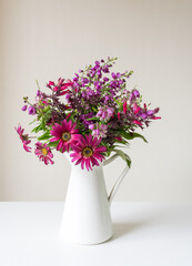 Vertical close up of purple and red spring flowers in white jug on shelf against beige wall