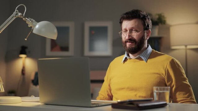 Angry man, rage emotion. Angry annoyed bearded man with glasses in home office looking at computer screen and violently slams his fist on desk and screams