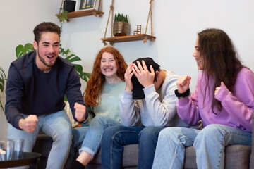 Excited friends cheering for team at critical moment. Man sitting on sofa and holding hands on head while his friends laughing and yelling, watching sports game on TV at home. Entertainment concept