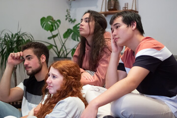 Disappointed friends sitting on sofa and watching football match. Sad multiethnic men and women upset about teams defeat. Sports fans spending time together at home. Losing, sports game concept