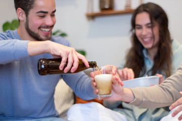 Happy man pouring beer into friends glasses at home. Smiling guy and women having fun together on weekend, drinking beverage while watching football match on TV. Entertainment, friendship concept