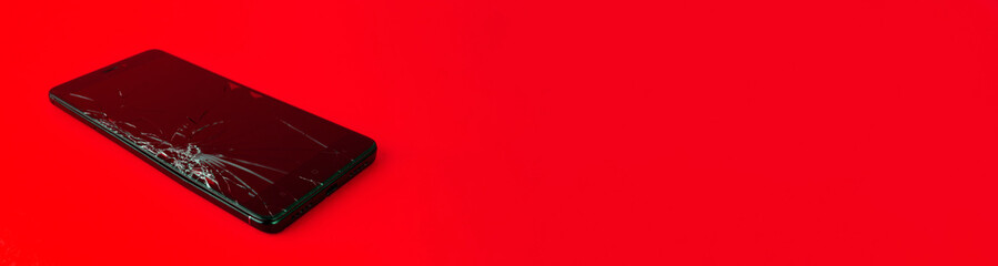 A mobile phone with a broken screen lies on a red background. A broken smartphone. Electronic...