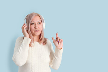 An adult woman in her 40s listens to music with wireless headphones and points her finger up while...