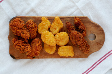 Tasty Fastfood: Chicken Nuggets, Wings and Tenders on a rustic wooden board, overhead view. Top view, from above, flat lay.