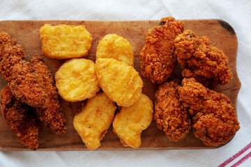 Tasty Fastfood: Chicken Nuggets, Wings and Tenders on a rustic wooden board, top view. Overhead, from above, flat lay. Close-up.