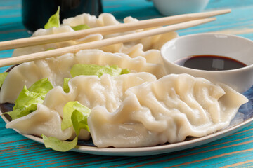 Close-up view of fresh boiled Chinese dumplings with soy sauce on blue wooden background. Selective focus.