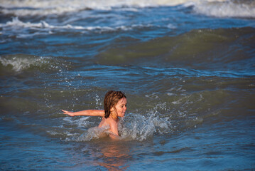 Happy kids have fun in sea on beach. Blue ocean with white big wawes on the background. Kid swimming in sea with wawes.