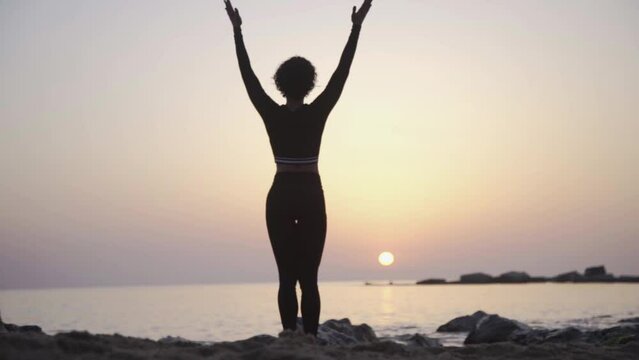 Silhouette of afro woman doing yoga asana at morning sunrise in the beach with ocean view. Healthy meditative lifestyle