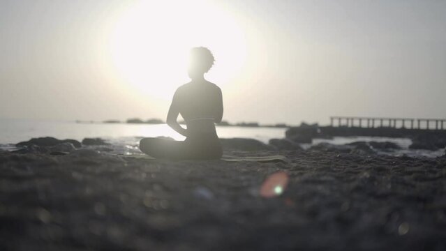 Afro American woman sitting in meditation contemplative blissful state of mind on ocean beach during a morning scenic sunrise