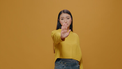 Asian woman doing rejection gesture with hand in front of camera, concept of refusing and not accepting. Person showing stop sign with palm, being in denial and expressing restriction.