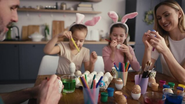 Zoom out of caucasian family of four people chatting and decorating easter eggs in domestic kitchen. Shot with RED helium camera in 8K   
