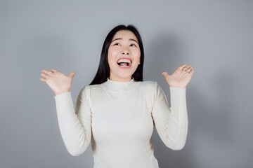 Asian woman in cream shirt funny shocked and surprise on gray background